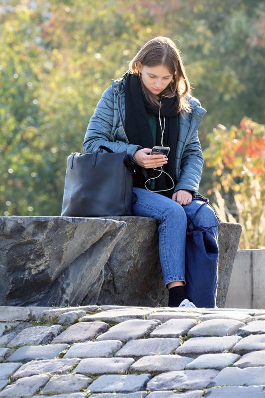 25 - Person wearing a blue puffer jacket and black scarf while using a smartphone